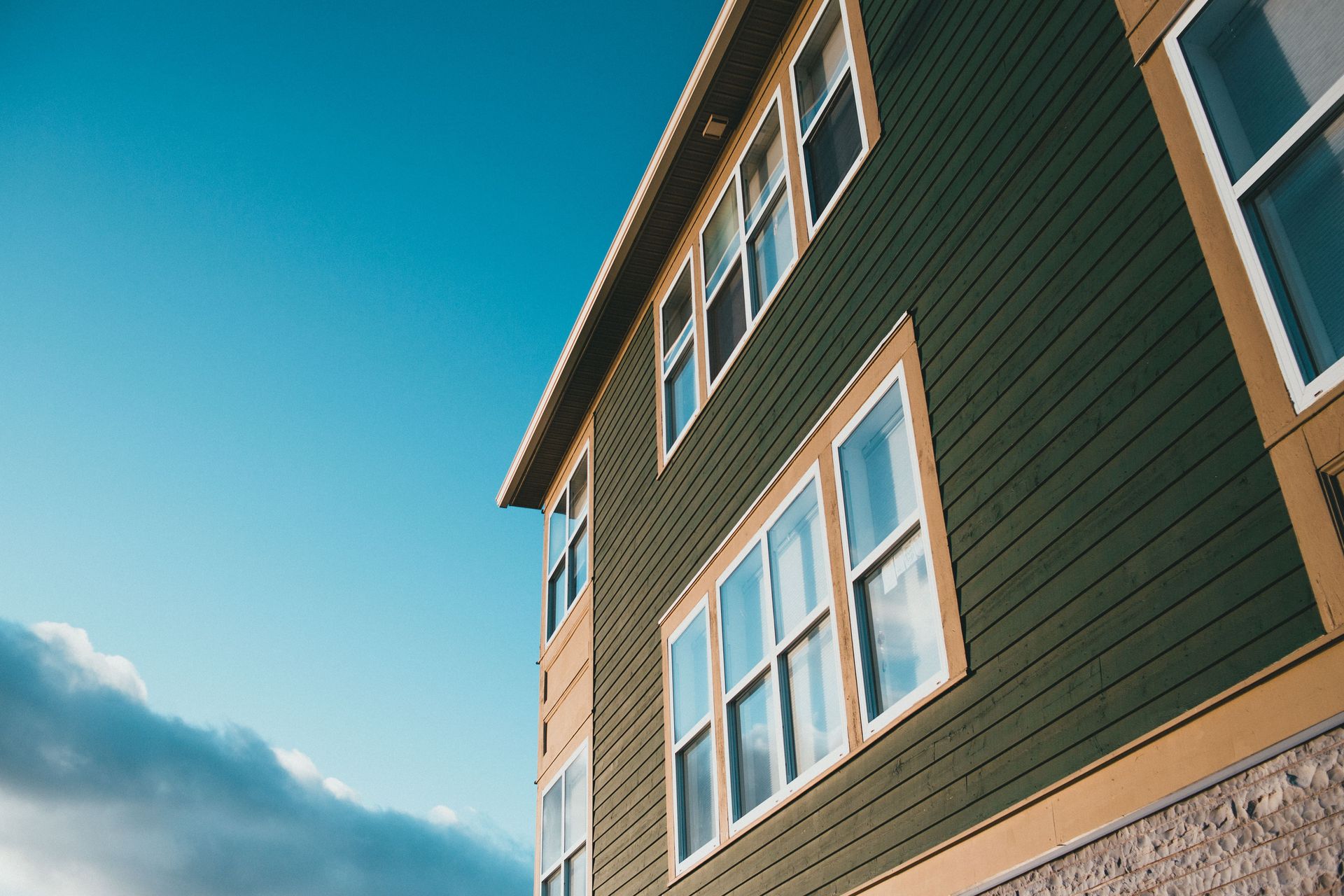 Low angle view of a green wooden house with multiple windows under a vibrant blue sky.